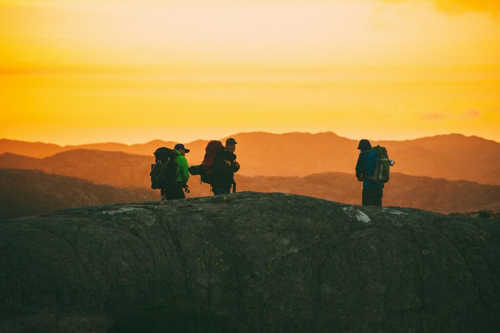 three hikers standing on cliff during golden time