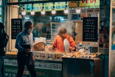 man in white dress shirt and black pants standing in front of food stall