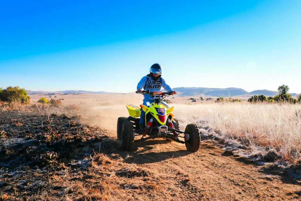 man riding blue and yellow atv on brown field under blue sky during daytime